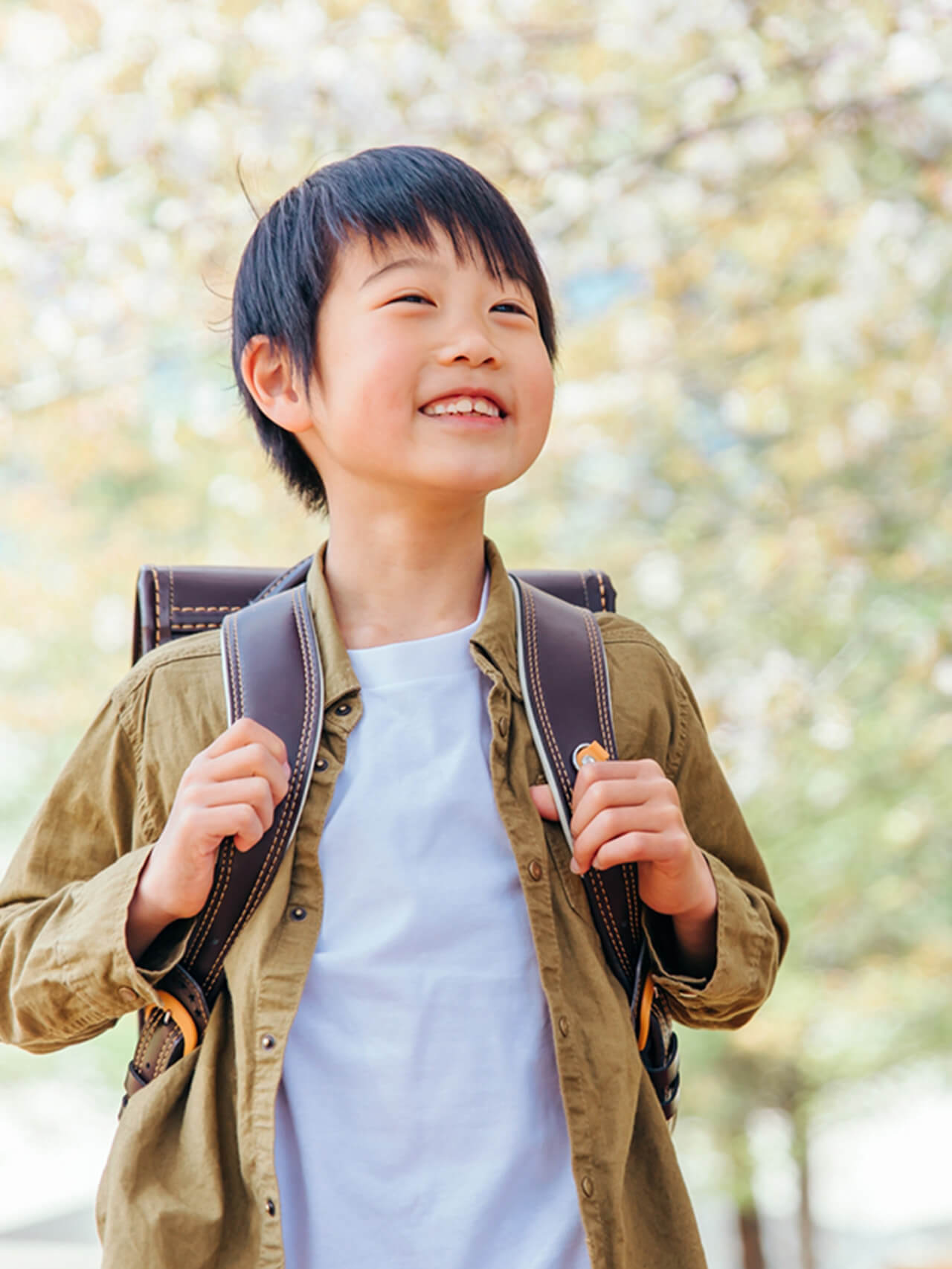 明るい屋外でランドセルを背負った男の子の笑顔の写真。