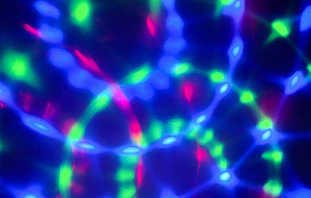 暗闇の中で、緑、青、赤の光が複雑に交差している抽象的な写真。